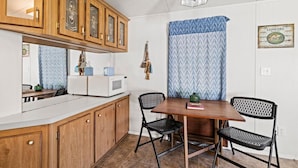 A compact kitchen with wooden cabinets, a microwave, and a dining table with chairs. - Magical Location on the River, Hiking, and Rafting (Sylva)