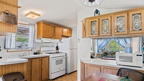 A compact kitchen with wooden cabinets, a stove, a microwave, and a dining area with a table and chairs. - Magical Location on the River, Hiking, and Rafting (Sylva)