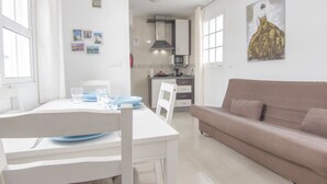 Un salon moderne avec une table à manger blanche, un canapé beige et une cuisine en arrière-plan.