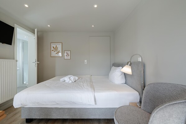 A neatly arranged bedroom with a bed, bedside lamp, and a chair. - Appartement Muschel (Westerland)