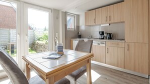 Une cuisine moderne avec des meubles en bois, une table à manger avec des chaises et une vue sur l’extérieur.
