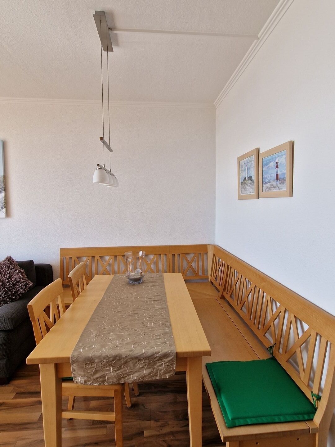 Un comedor con una mesa de madera y bancos, una lámpara colgante y dos cuadros en la pared.