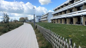 Ein Weg führt zu einem modernen Gebäude mit flachem Dach und mehreren Balkonen.