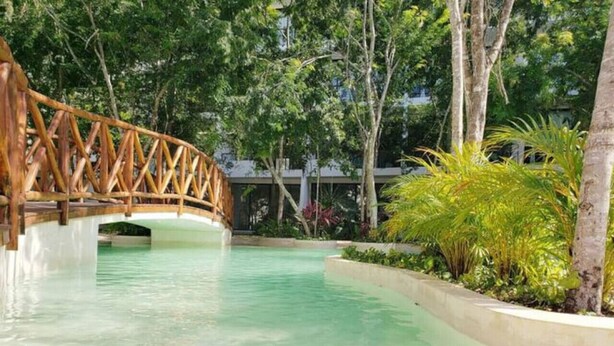 Une piscine aux eaux cristallines, traversée par un pont en bois, et entourée d’une végétation luxuriante.