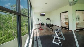 Une salle de sport moderne, équipée de matériel d’exercice, dotée de grandes fenêtres et offrant une vue sur la verdure.