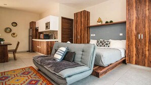 Un espace de vie compact comprenant un canapé, un lit, une kitchenette et des meubles de rangement en bois.
