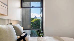 Quarto com uma janela grande, uma cama com manta branca e uma planta.