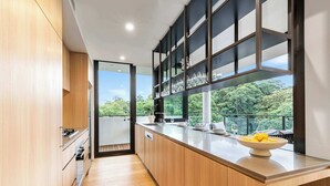 Cozinha moderna com armários de madeira, uma janela grande e vista para o verde.