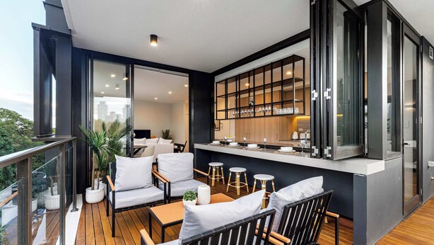 Uma área de estar moderna ao ar livre com deck de madeira, assentos e bancada de cozinha.