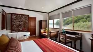 Un dormitorio con una cama grande, un escritorio, una silla, un ventanal con vistas a zonas verdes y un armario de madera.