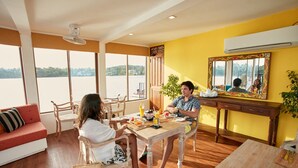 Un comedor con mesa de madera, sillas y sofá. Se observa un ventanal con vista a una masa de agua.