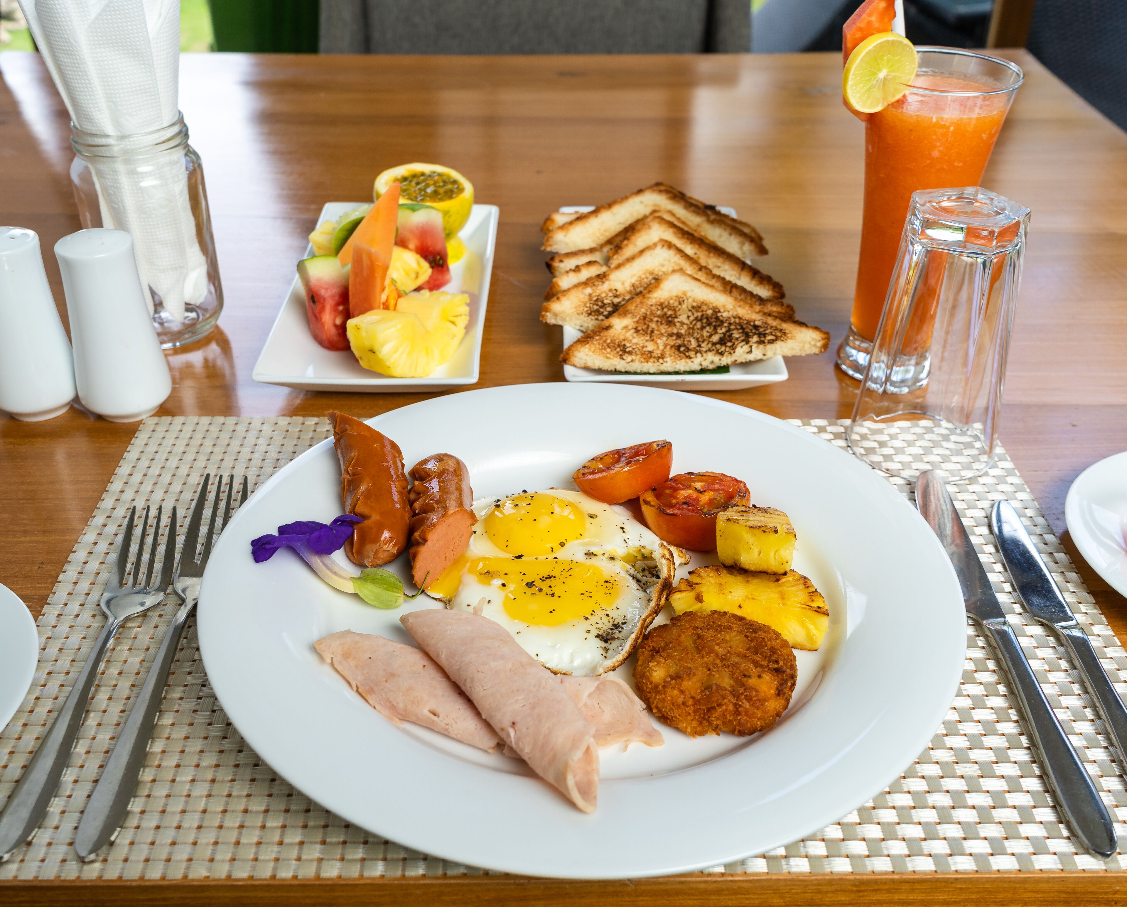 Un piatto con uova, prosciutto e pane tostato, un piatto di frutta e un bicchiere di succo d'arancia.