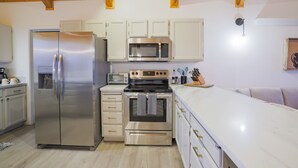 Een moderne keuken met roestvrijstalen apparatuur, houten balken in het plafond en witte keukenkastjes.