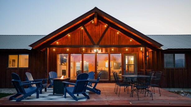 Een houten hut met een terras, buitenmeubels en grote ramen.
