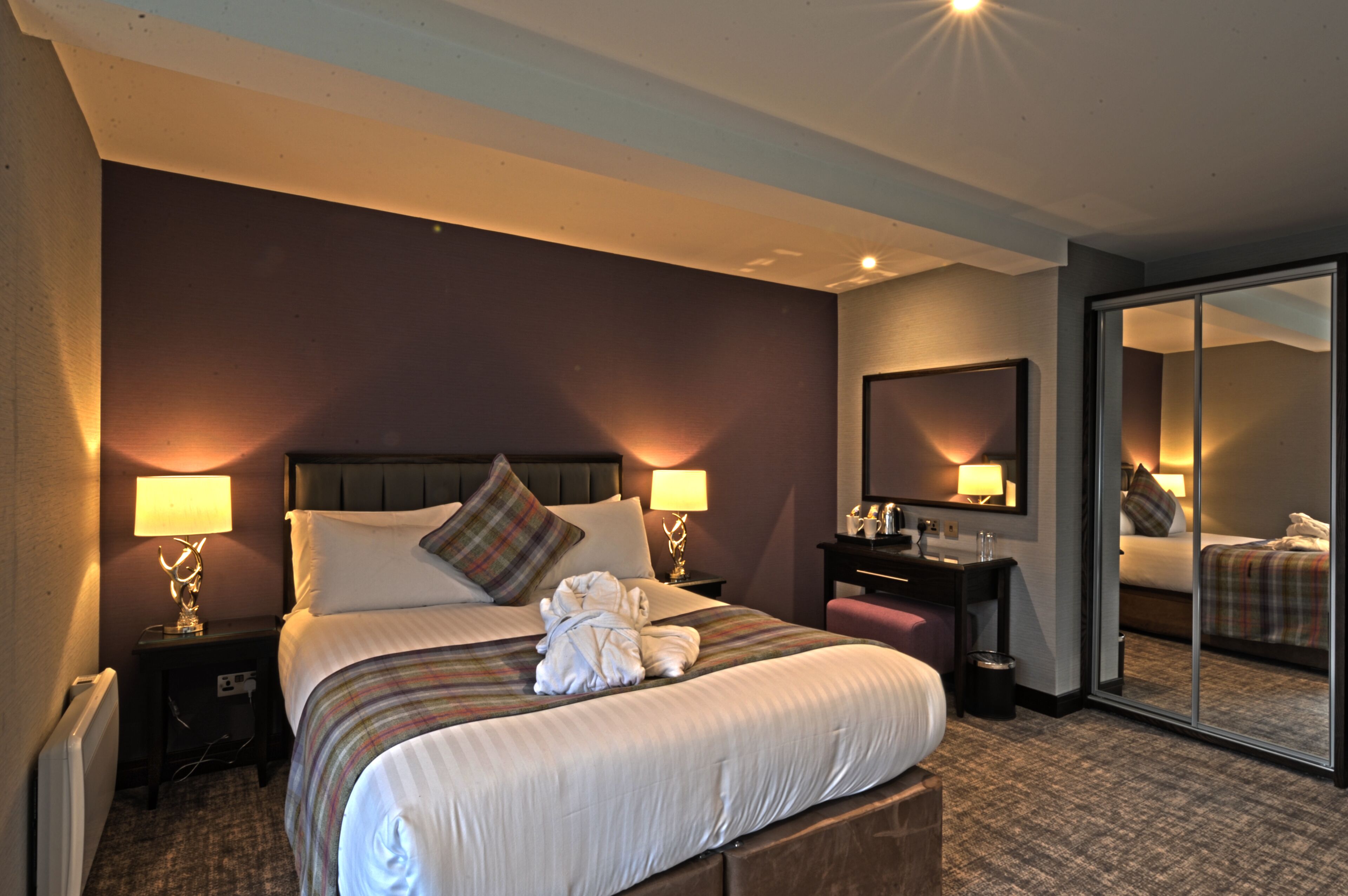 A hotel room with a large bed, two bedside tables with lamps, a mirror, a small desk, and a sliding door leading to another room.