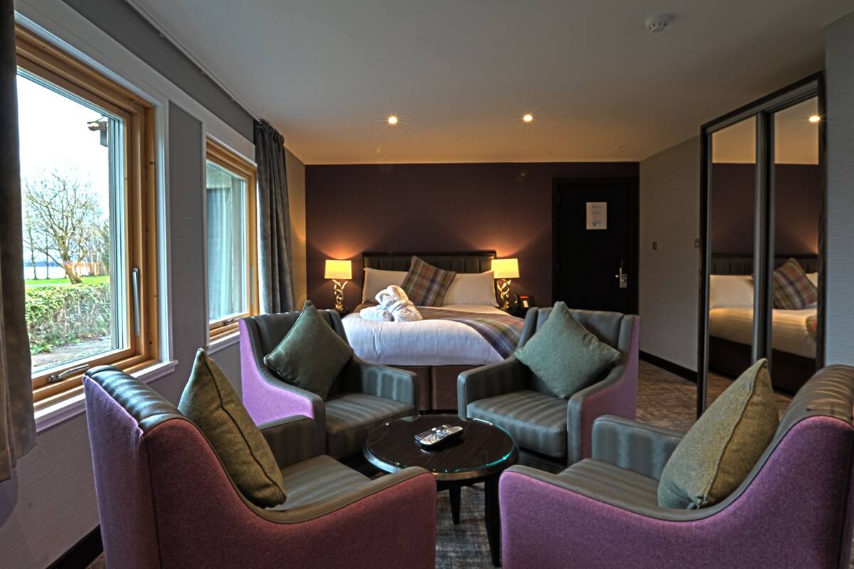 A hotel room with a bed, two armchairs, a coffee table, and a large window.