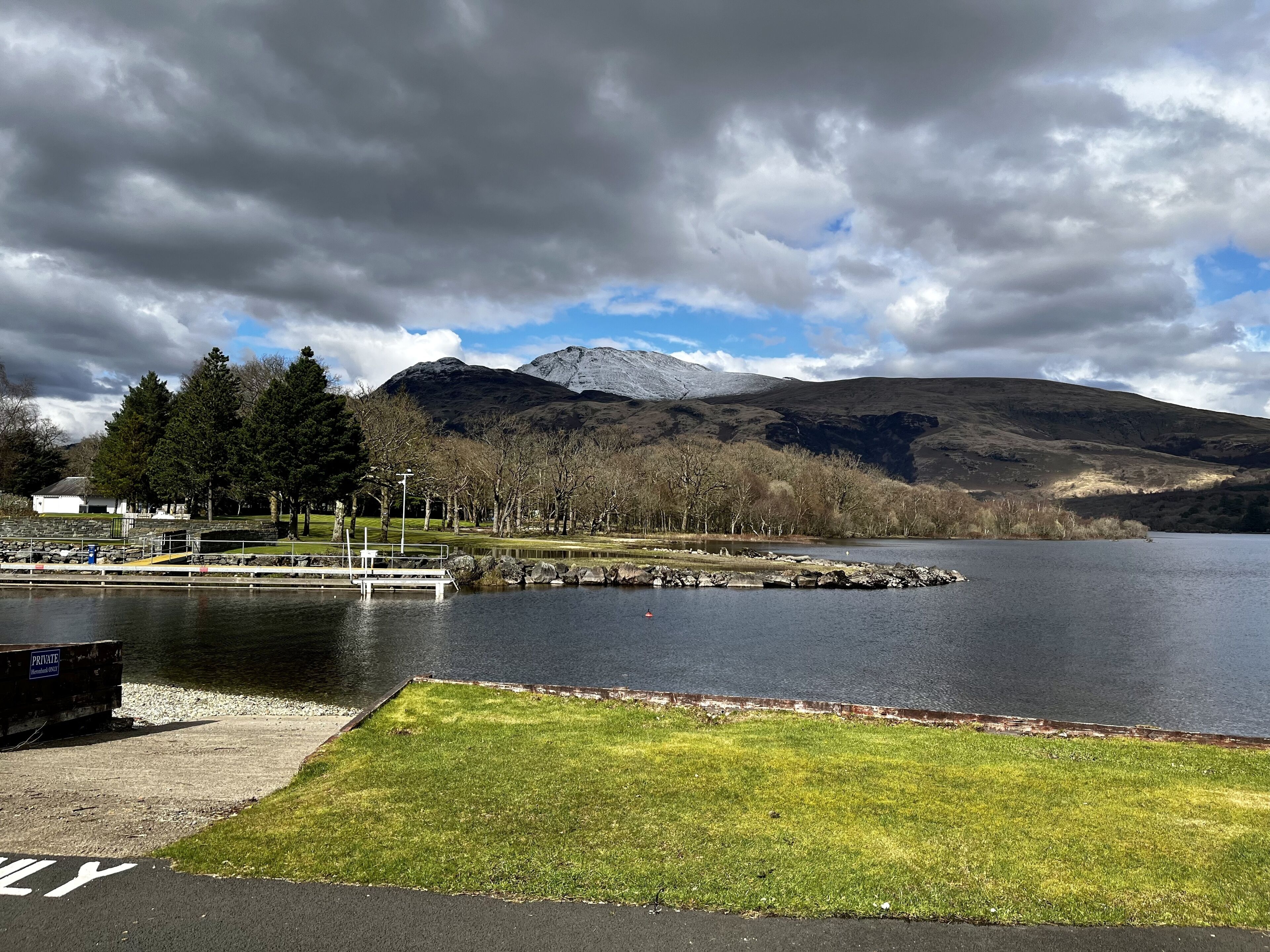 Un lago con un muelle, una zona de césped y una montaña al fondo.