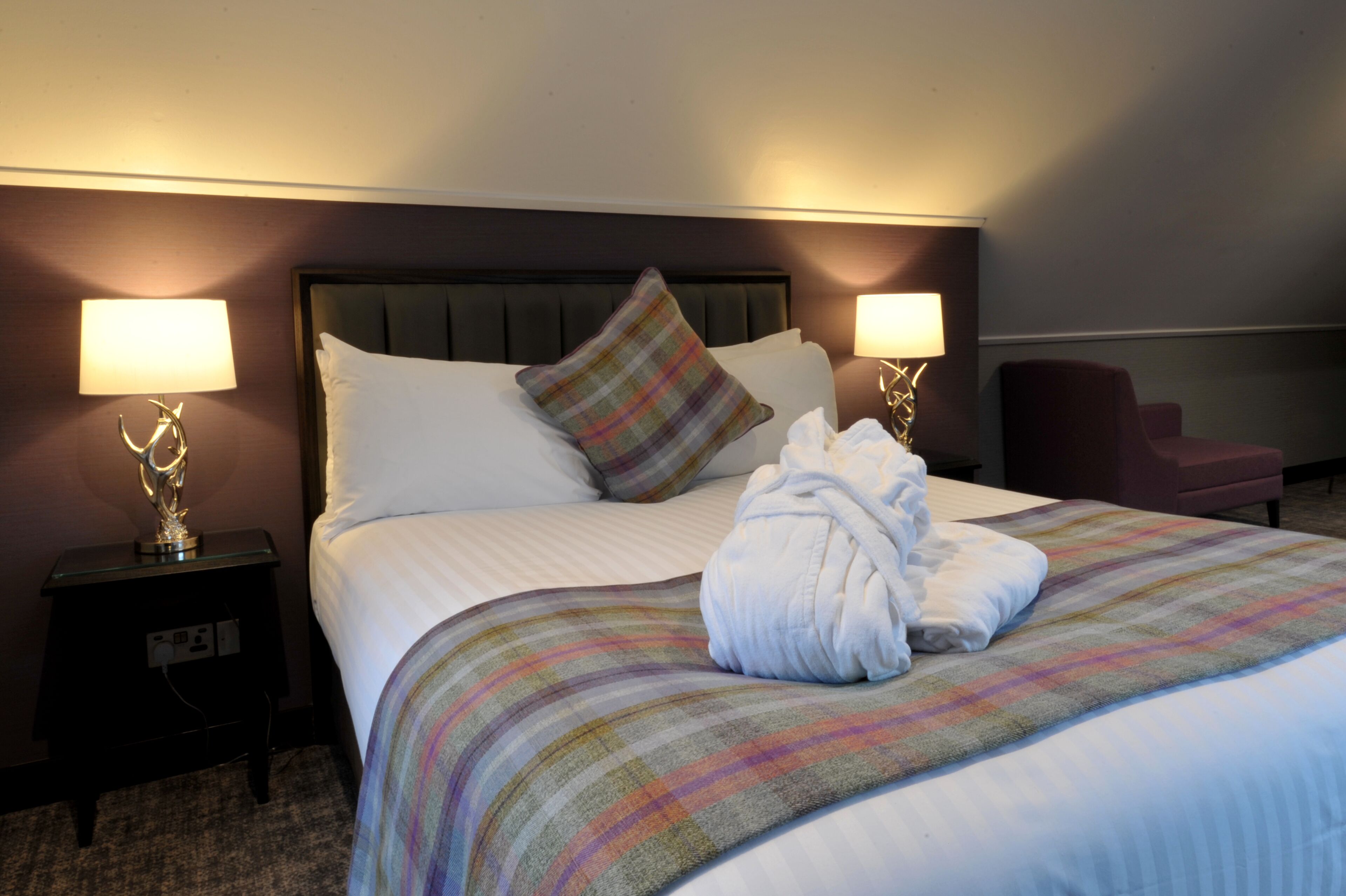 A neatly made bed with a striped blanket, two bedside lamps, and a robe on the bed.