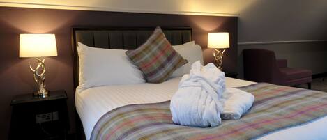 A neatly made bed with a striped blanket, two bedside lamps, and a robe on the bed.