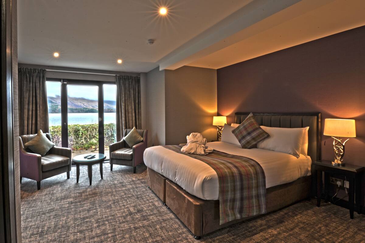 A hotel room with a large bed, two armchairs, a small table, and a view of the sea.