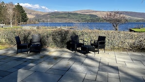 A patio with outdoor seating and a view of a lake and mountains. - The Beach House (Alexandria)