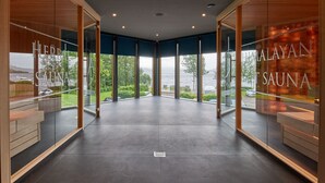 A modern spa interior with large glass doors, a view of the sea, and a sign for 'Herbal Sauna'. - The Beach House (Alexandria)