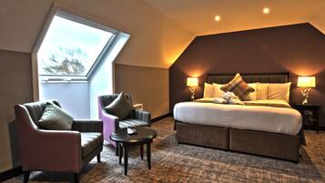 A hotel room with a large bed, two armchairs, a small table, and a skylight.