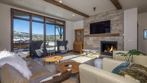 A spacious living room with a fireplace, large windows, and a view of a snowy landscape. - Penthouse | Close to Shuttle | Hot Tub (Big Sky)