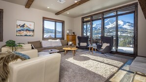 A spacious living room with a large window offering a mountain view, a cozy sofa, a coffee table, and modern chairs. - Penthouse | Close to Shuttle | Hot Tub (Big Sky)