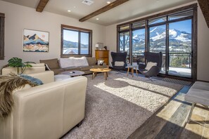 A spacious living room with a large window offering a mountain view, a cozy sofa, a coffee table, and modern chairs. - Spend Summer in Big Sky! Condo with Lone Peak Views (Big Sky)
