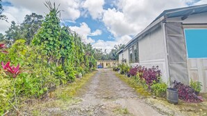 A pathway leading to a building with a corrugated metal roof and a blue door. - Hotel O Susupuan KostNearTaman Deki Lestari (Tondano)