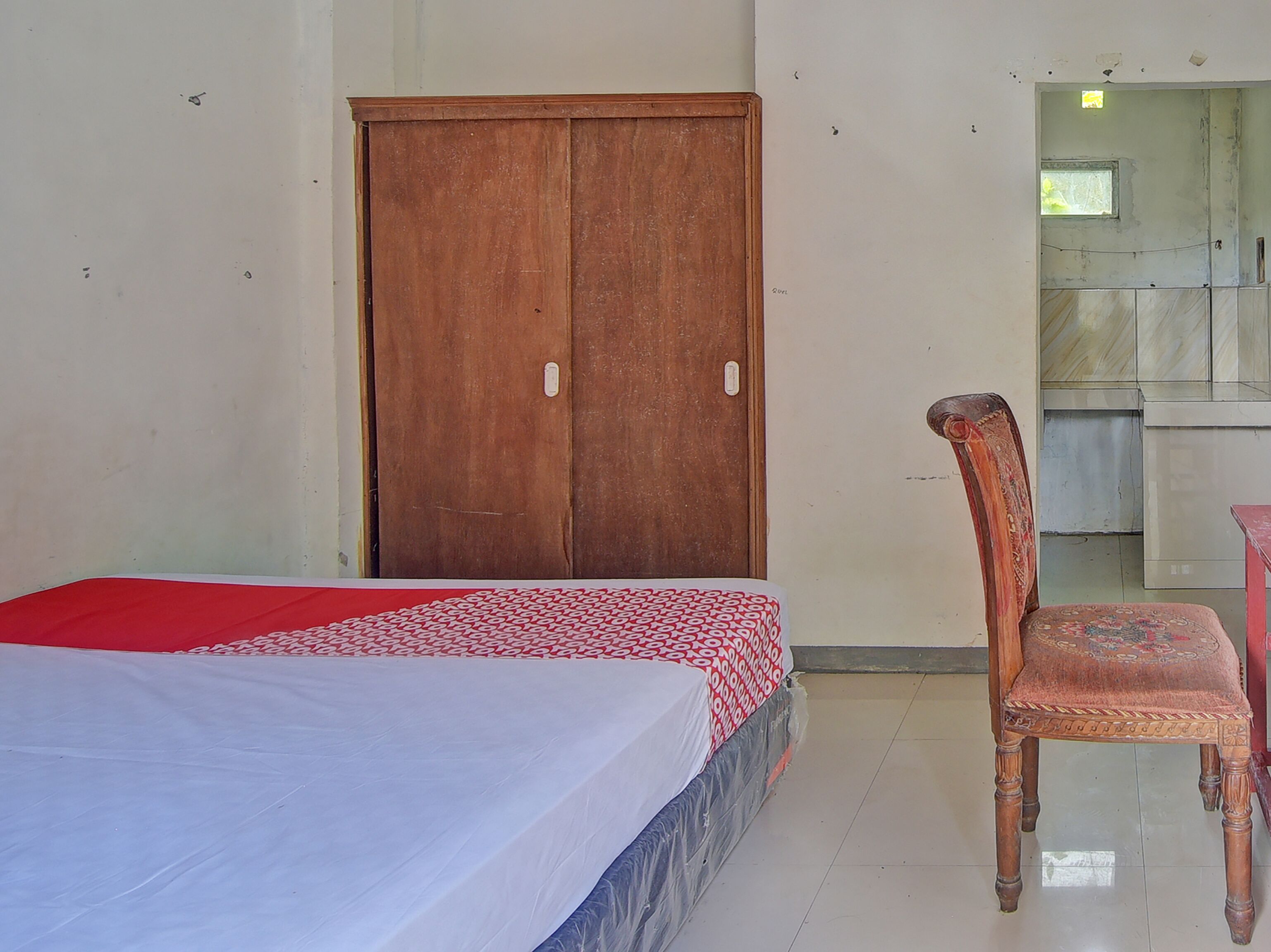 Una habitación con una cama, un armario de madera, una silla y una mesita.