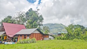 A rural village with traditional houses, a green field, and a mountain in the background. - Hotel O Susupuan KostNearTaman Deki Lestari (Tondano)