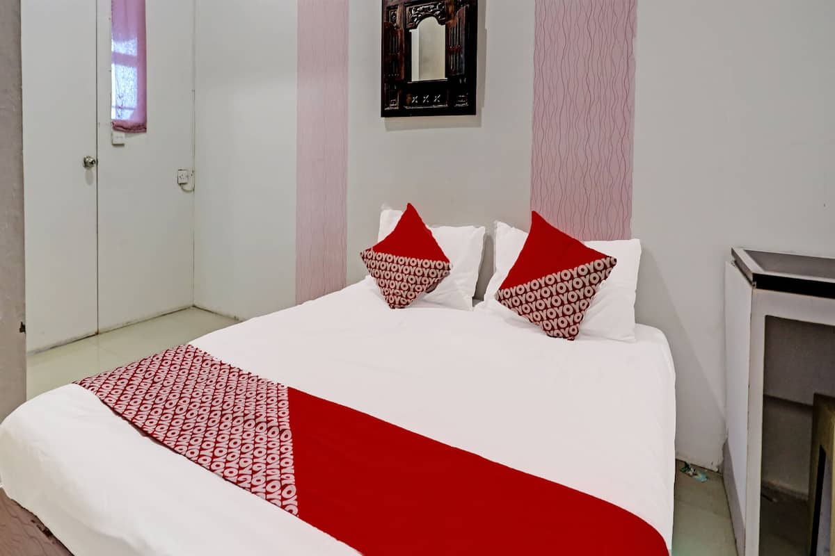 A hotel room with a neatly made bed, a small bedside table, and a wall-mounted mirror.