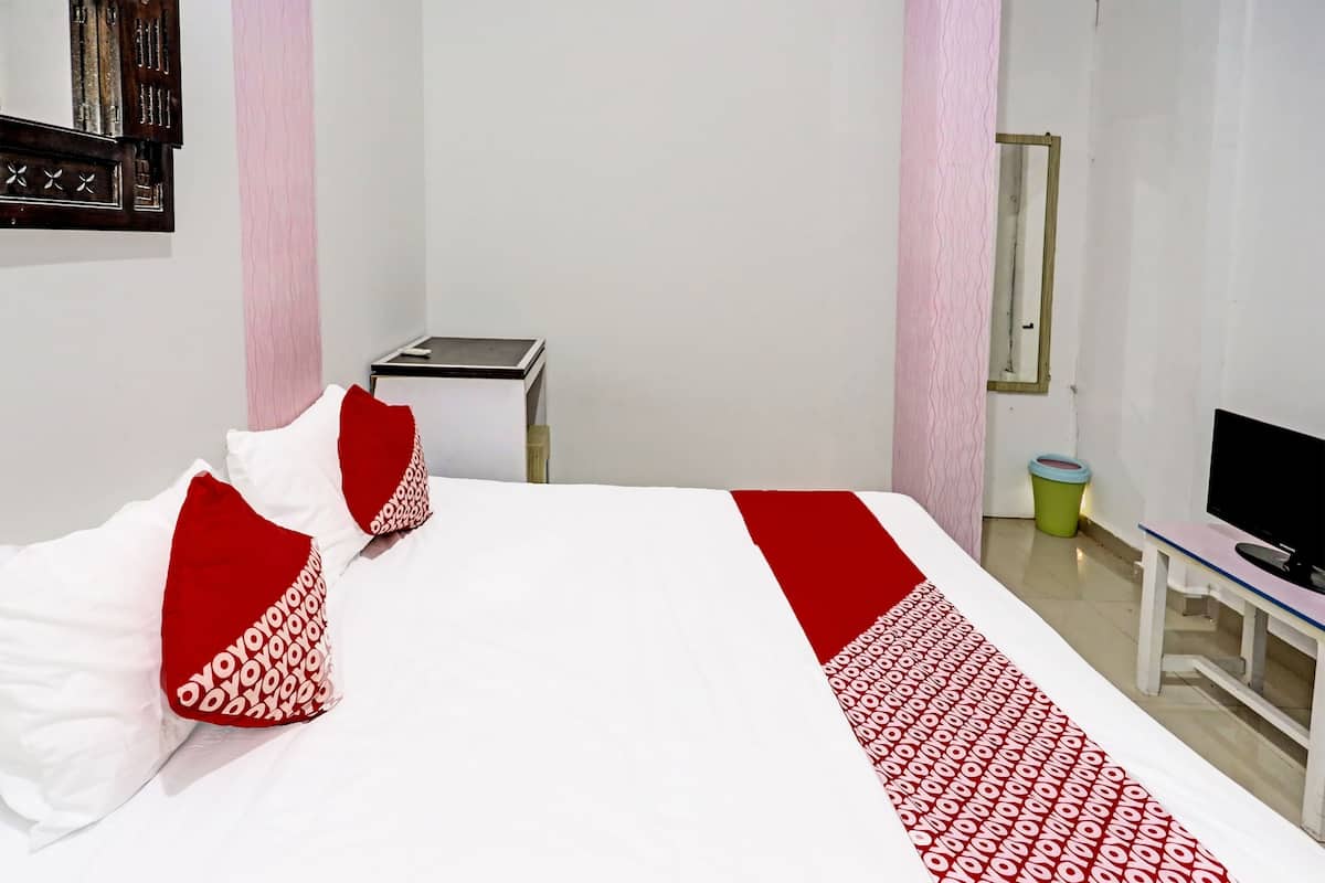 A hotel room with a bed, pillows, a bedside table, a television, and a trash bin.