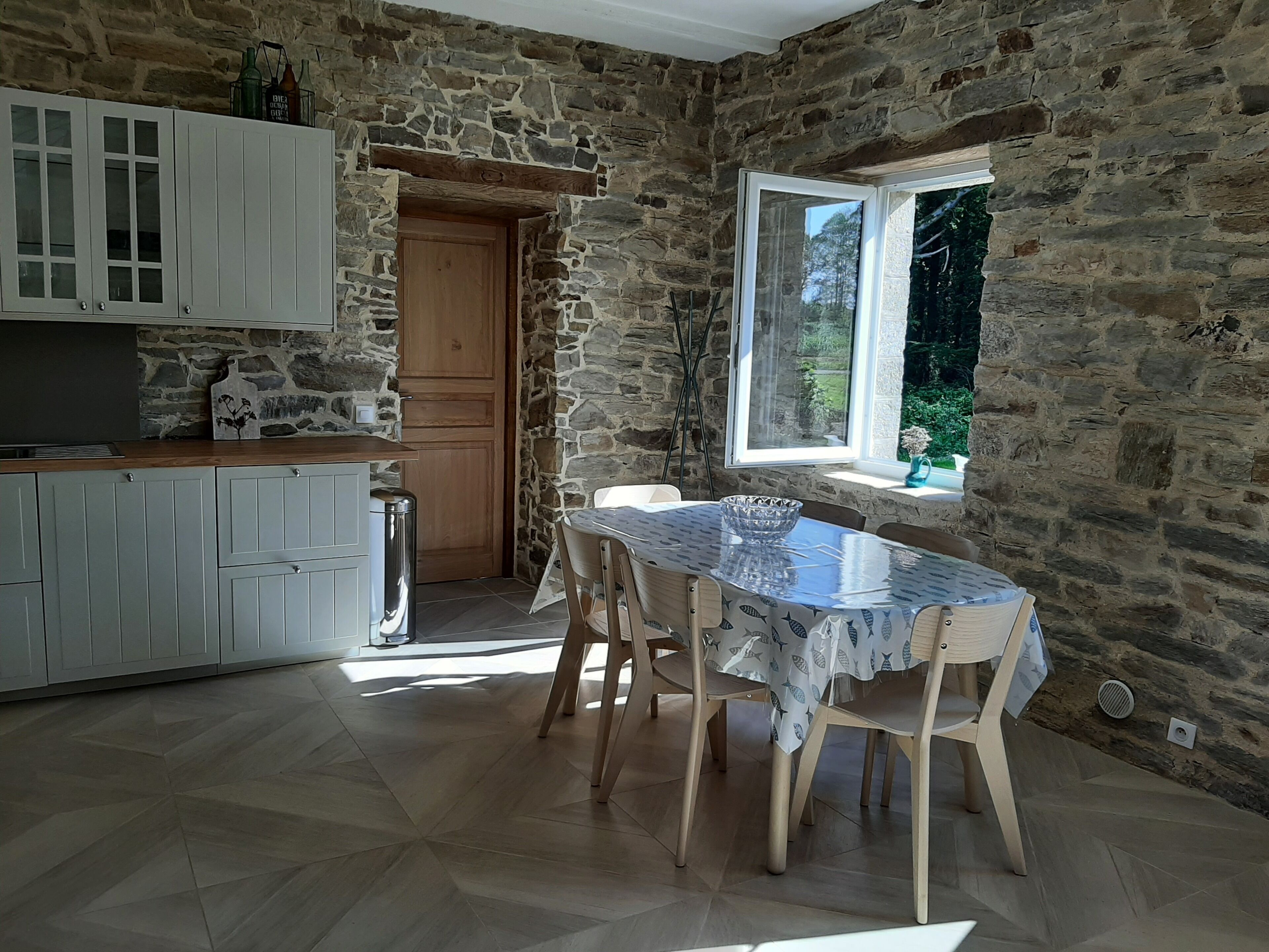 Een keuken met stenen muren, een houten deur en een eethoek met een tafel en stoelen.