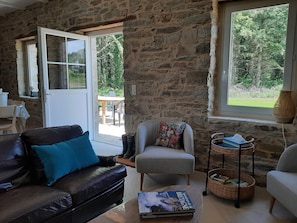 Una habitación con paredes de piedra, un sofá de cuero, un sillón gris y una mesa de centro con un libro.