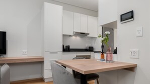 A modern kitchen with white cabinets, a wooden dining table, and a grey chair. - The Carrington 401 (Cape Town)