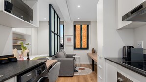 A modern kitchen with a dishwasher, a coffee machine, and a dining area with a sofa and table. - The Carrington 401 (Cape Town)