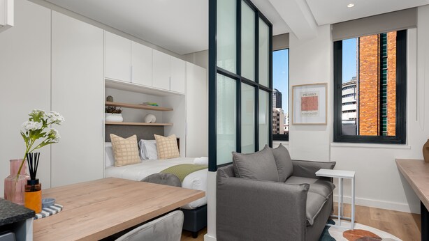 A modern, compact living space with a kitchenette, a grey sofa, a small dining table, and a large window offering a view of the city. - The Carrington 401 (Cape Town)