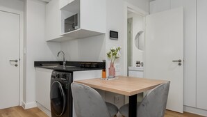 A compact kitchen with a washing machine, a wooden table, and two grey chairs. - The Carrington 401 (Cape Town)