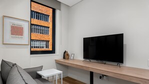 A modern living room with a grey sofa, a white side table, a TV on a wooden stand, and a framed artwork on the wall. - The Carrington 401 (Cape Town)
