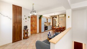 A modern kitchen with a dining area, a staircase, and a living room with a sofa and a TV.