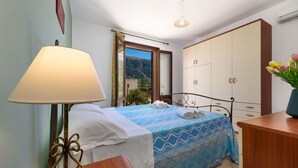 A bedroom with a bed, a nightstand, a lamp, a wardrobe, and a view of the outdoors.