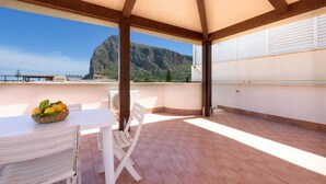 A covered outdoor area with a table and chairs, a basket of lemons, and a view of a mountain.