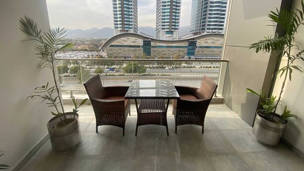 A balcony with a table and chairs, potted plants, and a view of tall buildings and a bridge. - Luxurious Apartment with Fascinating Margalla View (Islamabad)
