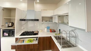 A modern kitchen with white cabinets, a gas stove, a microwave, and a stainless steel sink. - Luxurious Apartment with Fascinating Margalla View (Islamabad)