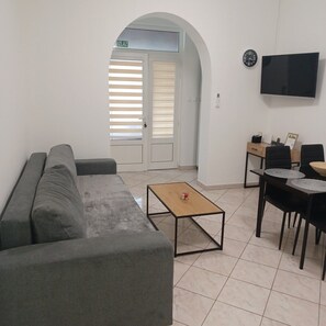 A living area with a sofa, a coffee table, a TV mounted on the wall, and a dining table with chairs. - Apartment Amko in Porec, Istria (Porec)
