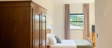 A bedroom with a bed, a wardrobe, a window with a view, and a ceiling fan.