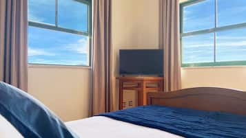 A hotel room with a bed, a TV on a stand, and large windows with curtains.